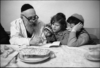 Moshe Shapiro teaching children prayers from the Hagaddah after Passover Seder in Warsaw's kosher kitchen. 1979